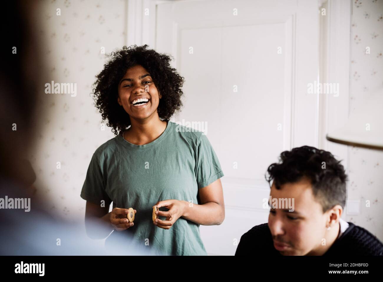 Ritratto di giovane donna allegra che tiene i biscotti mentre godendo con amico a casa Foto Stock