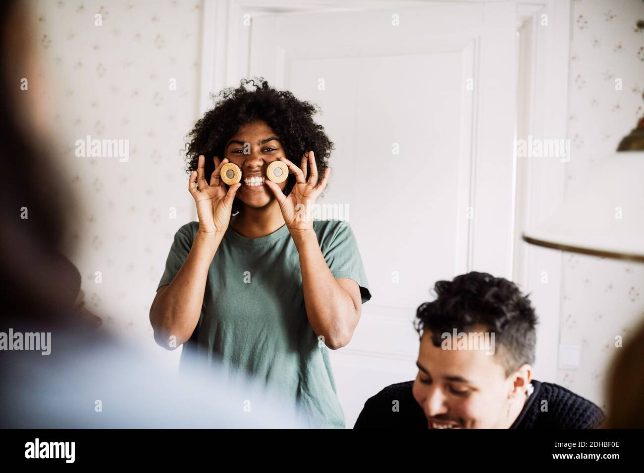 Ritratto di giovane donna sorridente che tiene i biscotti mentre godendosi con amico a casa Foto Stock