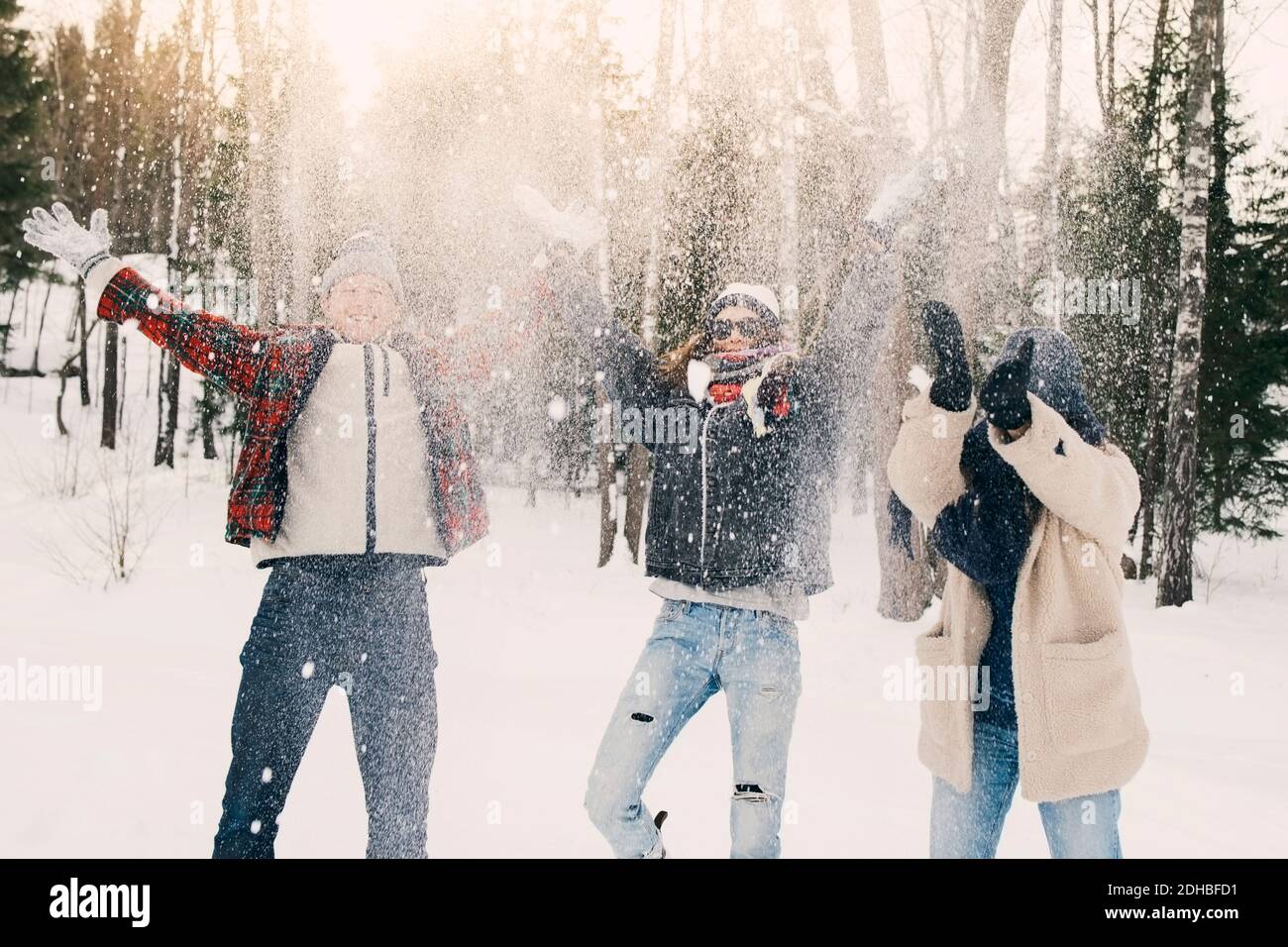 Amici giocosi che gettano la neve mentre si levano in piedi sul campo al parco Foto Stock