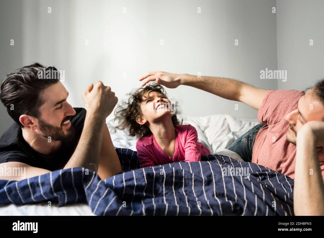 I padri che giocano con la figlia allegra mentre si sdraia sul letto a. casa Foto Stock