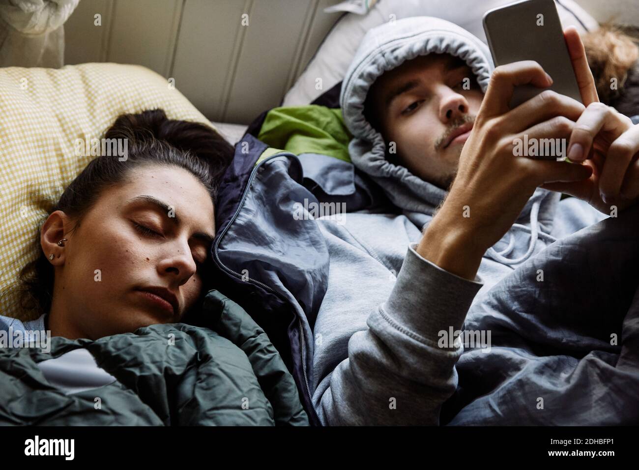 Visualizzazione ad alto angolo di un giovane uomo che utilizza il telefono cellulare mentre sdraiato da un amico a letto a casa Foto Stock