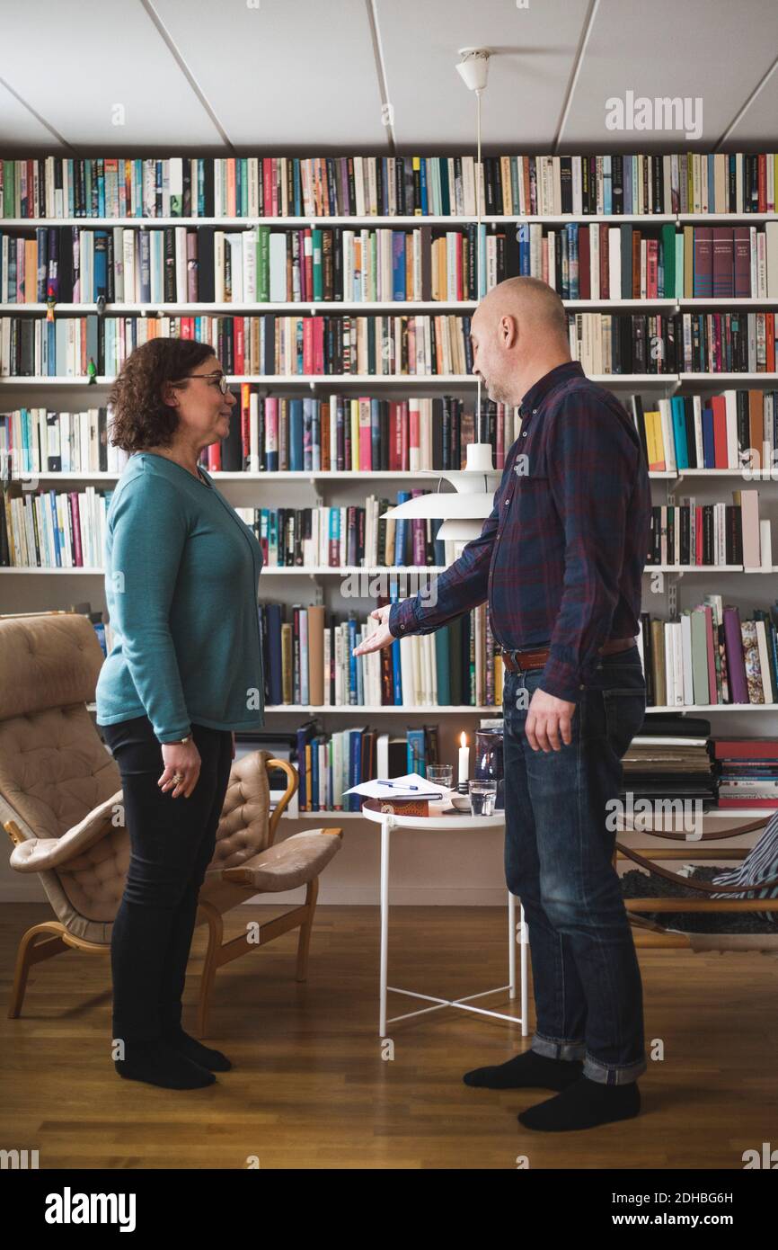 Lunghezza completa del terapeuta maschile gesturing mentre si parla con il paziente da libreria presso l'ufficio domestico Foto Stock