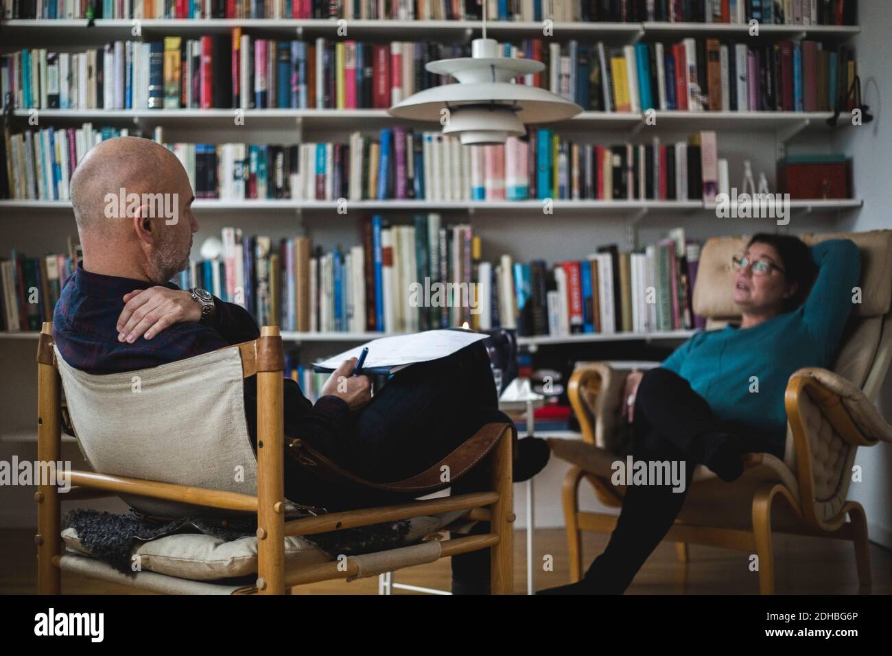 Terapeuta maschile che discute con paziente adulto femminile contro libreria a. ufficio domestico Foto Stock