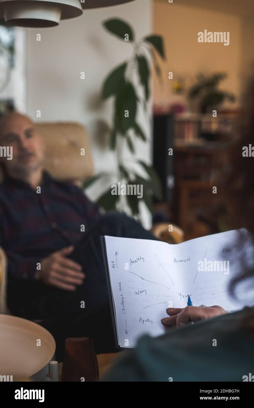 Terapista che tiene carta mentre discute con il paziente durante la sessione Foto Stock