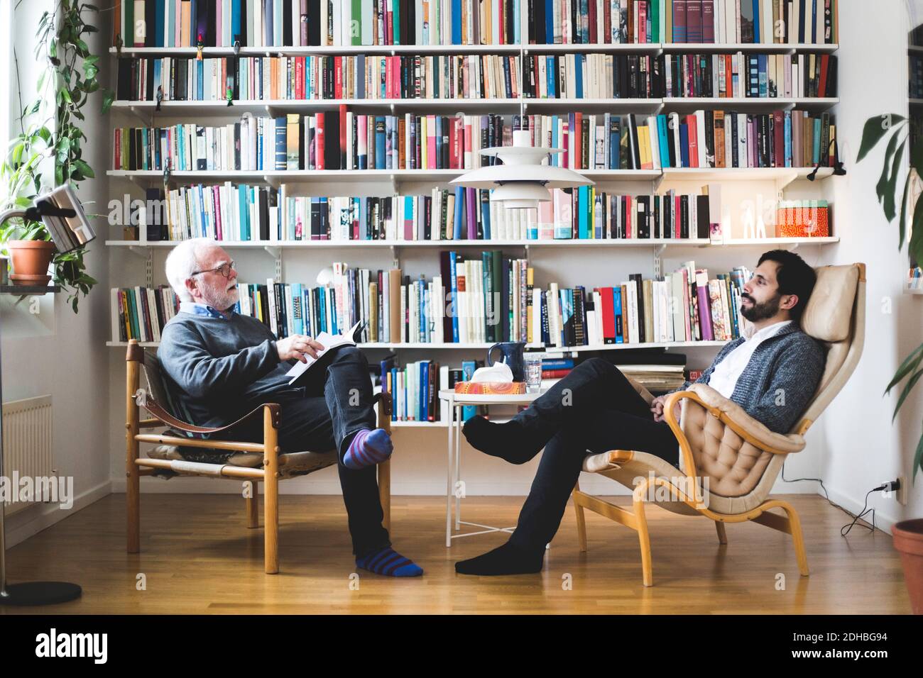 Terapista che comunica con l'uomo mentre si siede da scaffale libro a. ufficio domestico Foto Stock