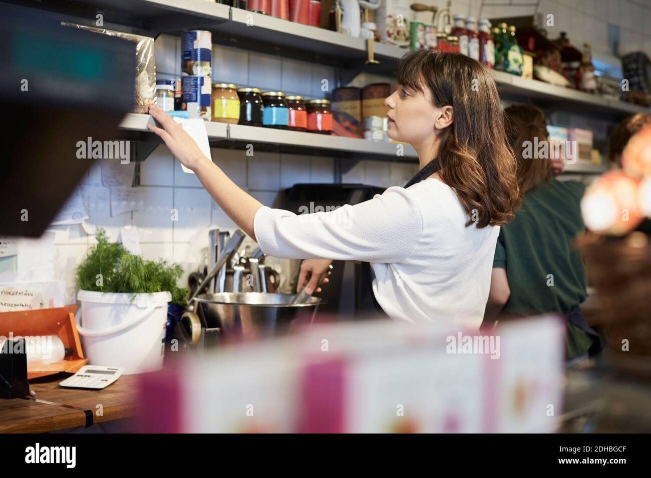 Donna proprietaria che organizza prodotti alimentari su scaffale in negozio Foto Stock