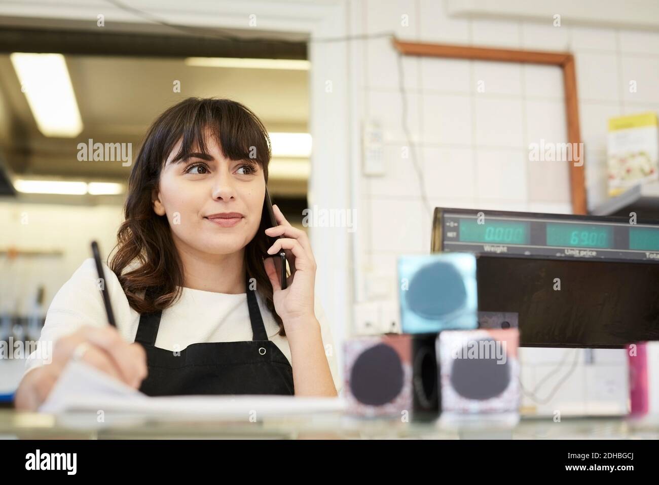 Donna proprietario sorridente mentre prendendo ordine attraverso il telefono cellulare a. banco in negozio Foto Stock