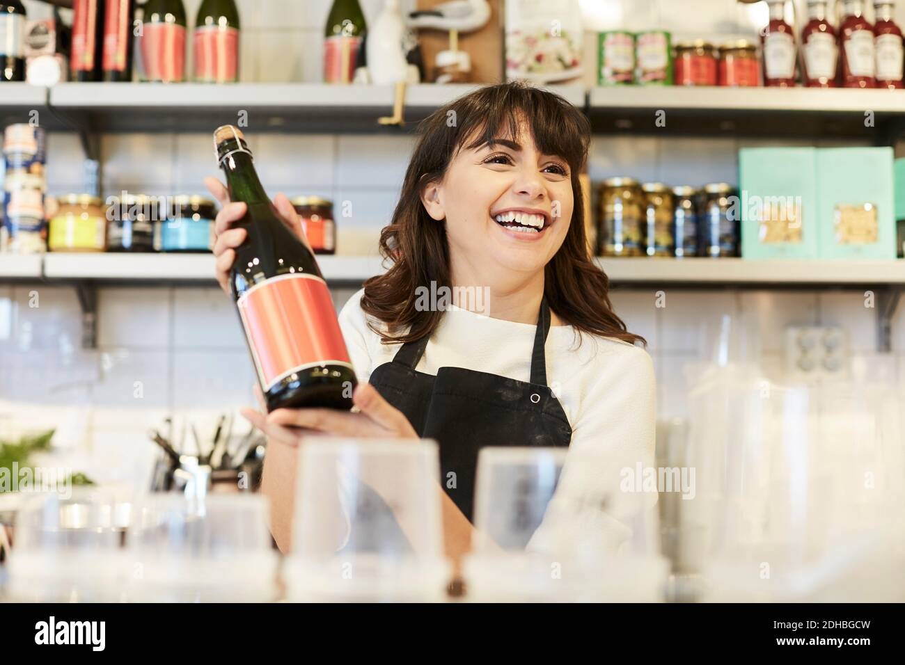 Donna felice proprietario che guarda via mentre tiene la bottiglia dell'olio a. banco in negozio Foto Stock