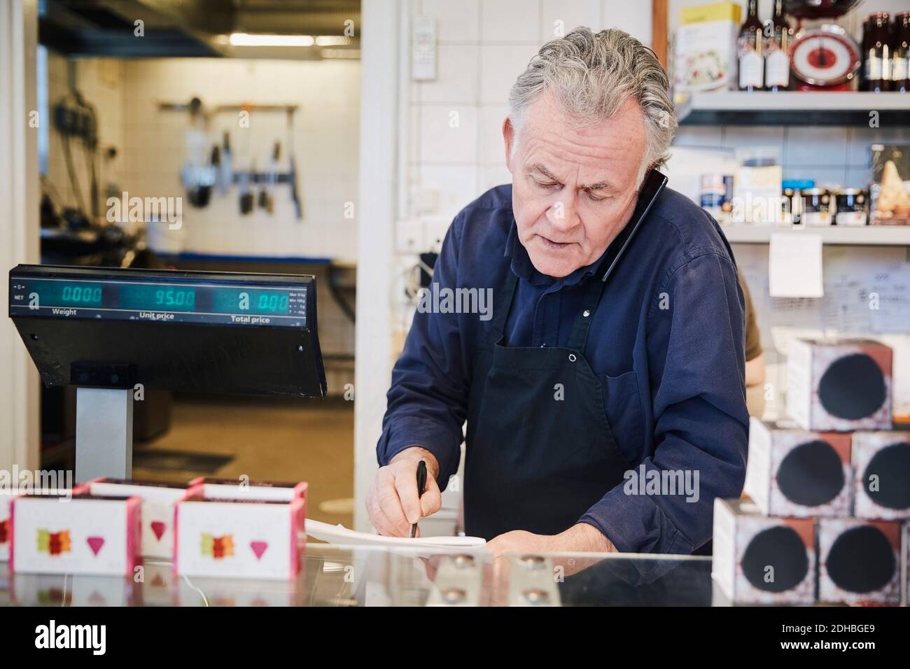 Il proprietario maschile che prende ordine anche se il telefono cellulare mentre si sta in piedi a. banco in negozio Foto Stock