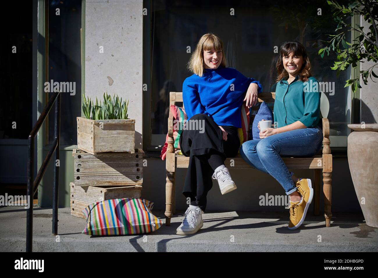 Ritratto a tutta lunghezza di sorridenti proprietari seduti sulla panchina all'esterno negozio Foto Stock