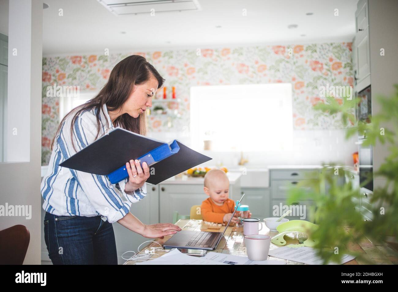 La madre che si sta occupando del multitasking mentre la figlia è seduta al tavolo da pranzo cucina Foto Stock