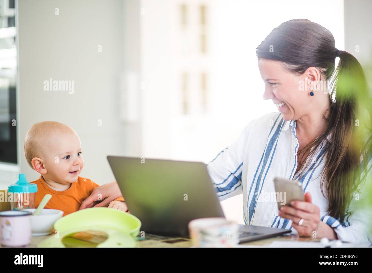 Donna d'affari allegra che gioca con la figlia mentre esegue il commercio da casa ufficio Foto Stock