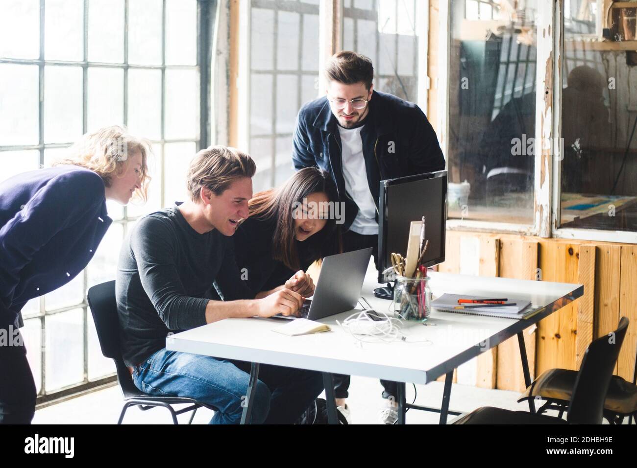 Curiosi colleghi che guardano al programmatore di computer maschile che codifica nel laptop sul posto di lavoro Foto Stock