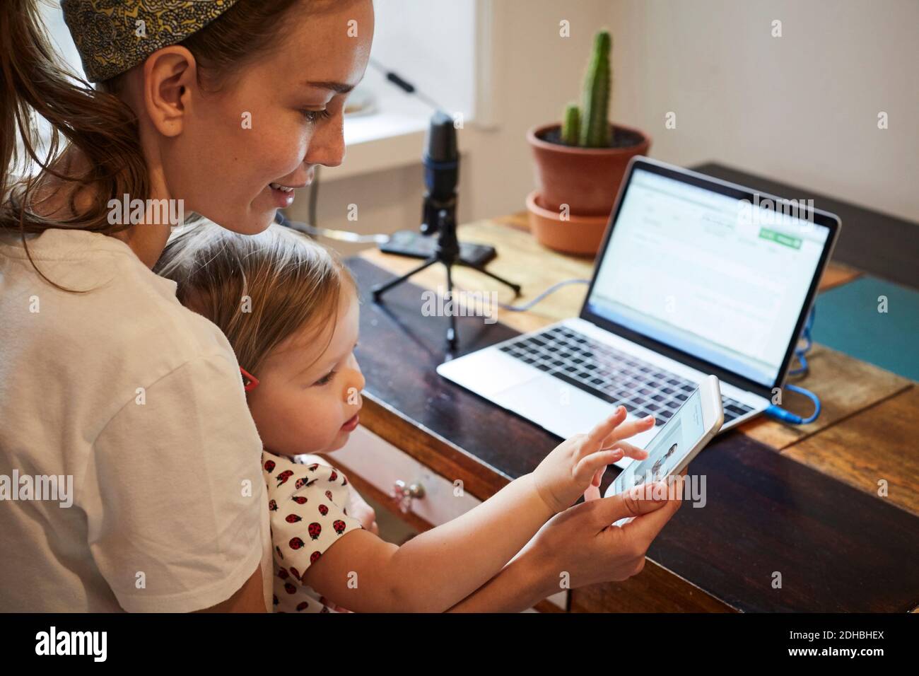 Podcaster che mostra il telefono cellulare a figlia mentre si utilizza il computer portatile AT casa Foto Stock