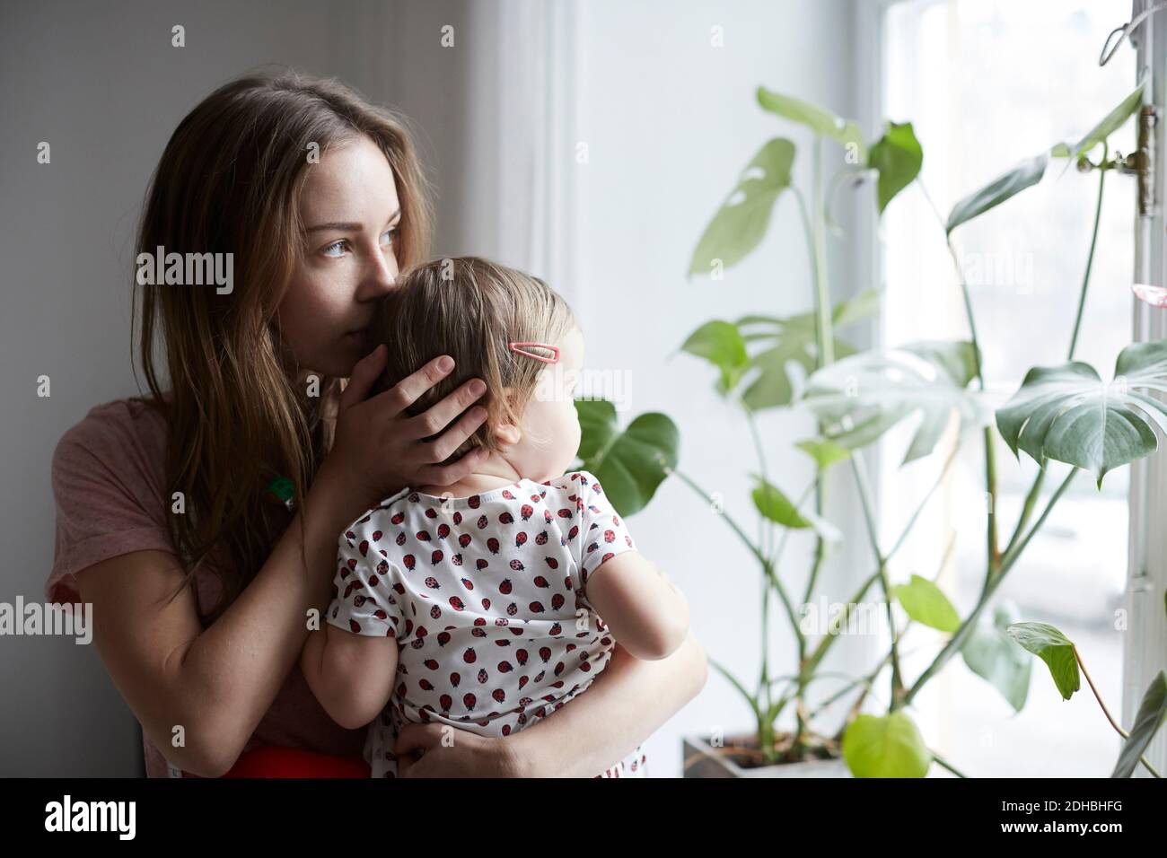 Madre baciando la figlia mentre si guarda attraverso la finestra a casa Foto Stock