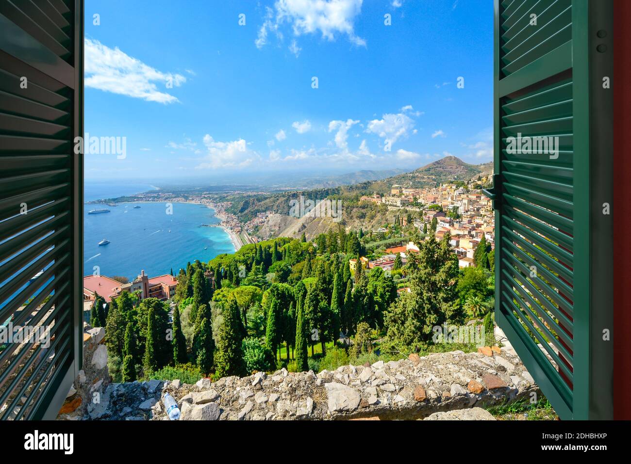 Vista attraverso una finestra aperta con persiane della costa e del villaggio di Taormina Italia, sull'isola della Sicilia nel Mar Mediterraneo Foto Stock