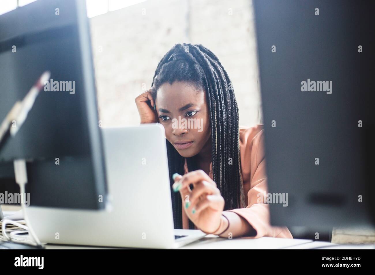 Esperto IT femminile serio che si concentra sui codici del computer durante l'uso laptop sul luogo di lavoro Foto Stock