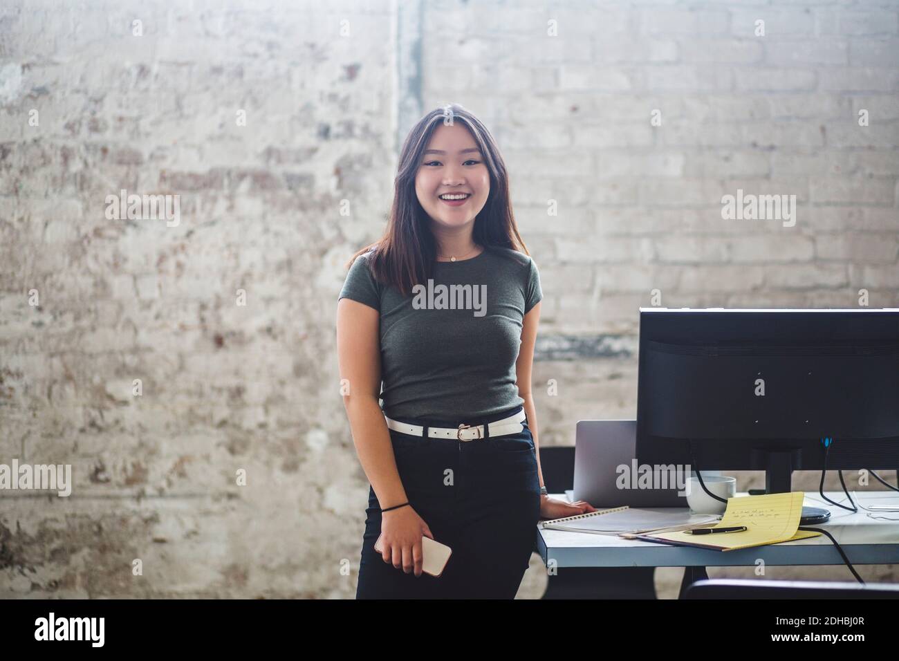 Ritratto di sorridente programmatore di computer femminile in piedi accanto alla scrivania a. ufficio creativo Foto Stock
