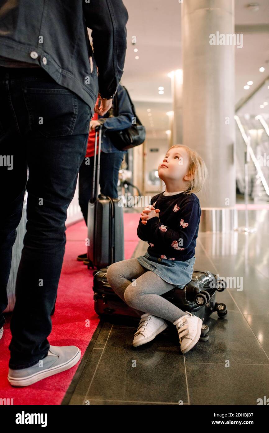 Tutta la lunghezza della ragazza con le mani aggrappate guardando il padre mentre si siede sulla valigia in hotel Foto Stock