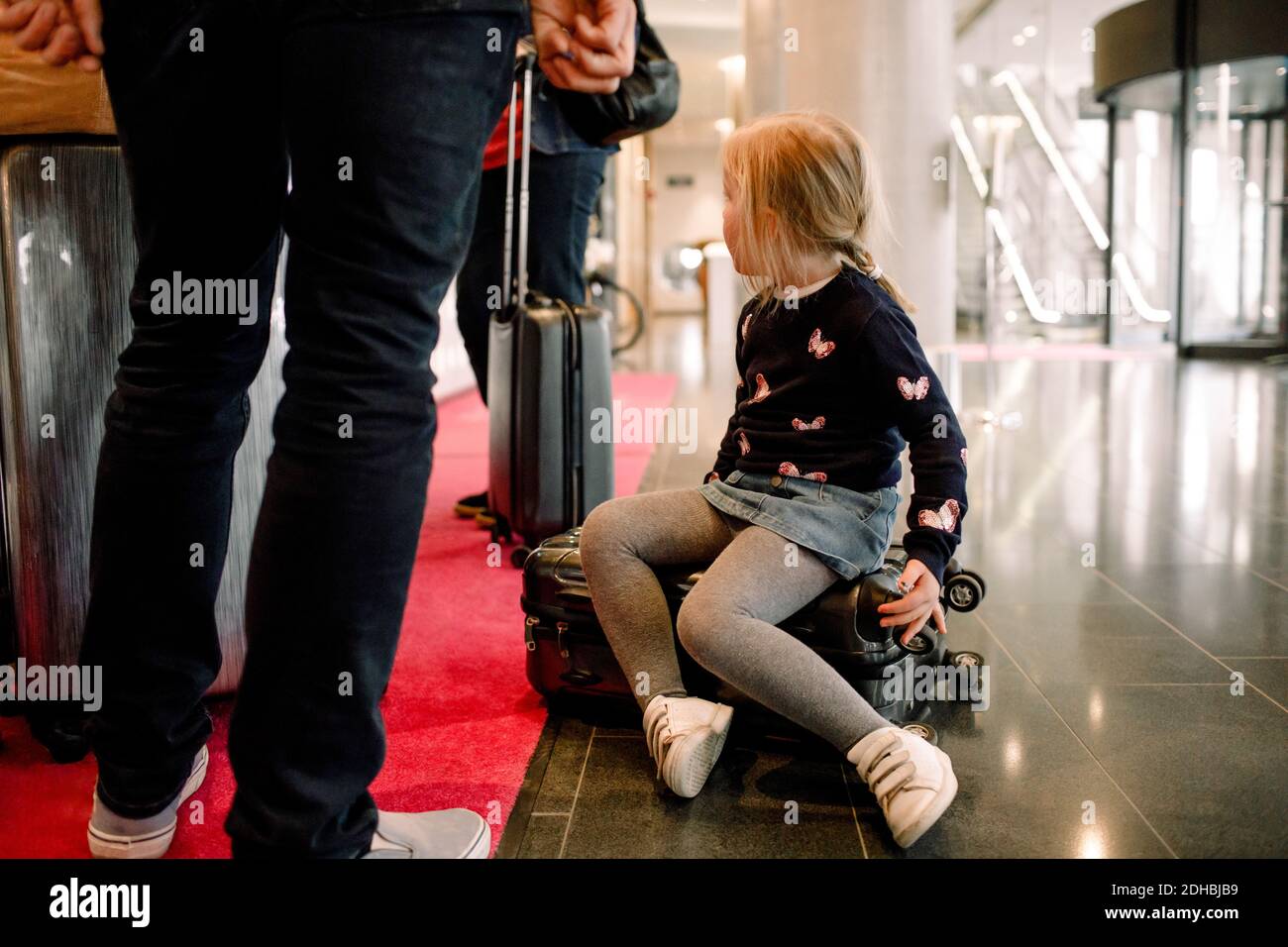 Ragazza seduta sulla valigia con la famiglia in piedi alla reception hotel Foto Stock