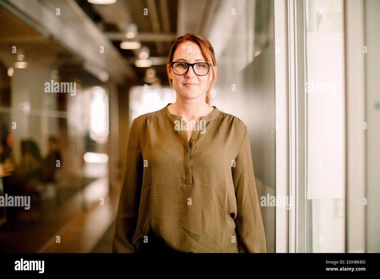 Ritratto di donna executive indossare occhiali e casual elegante mentre in piedi sul luogo di lavoro Foto Stock