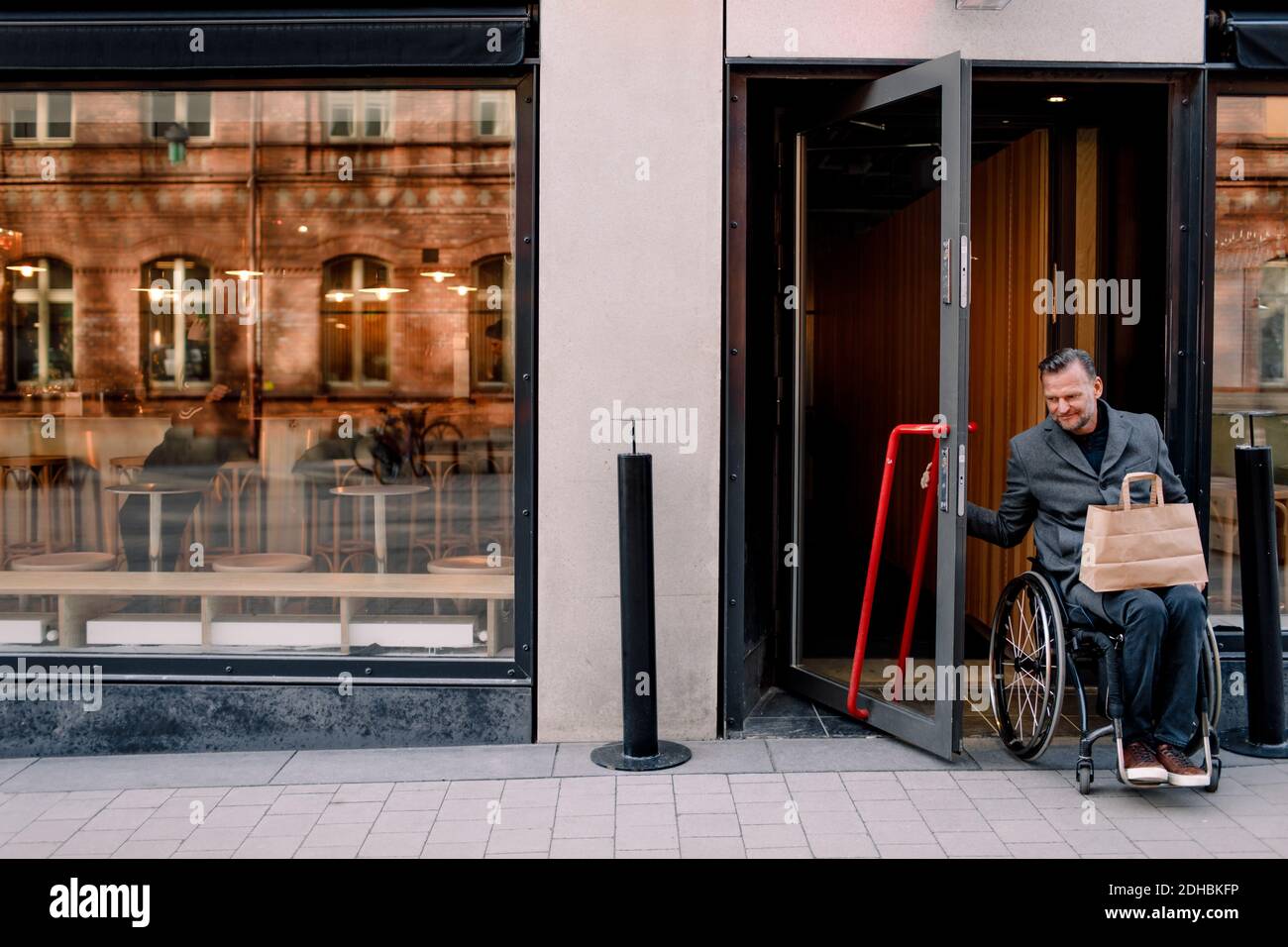 Uomo maturo per disabili con borsa per la spesa che lascia il negozio in città Foto Stock