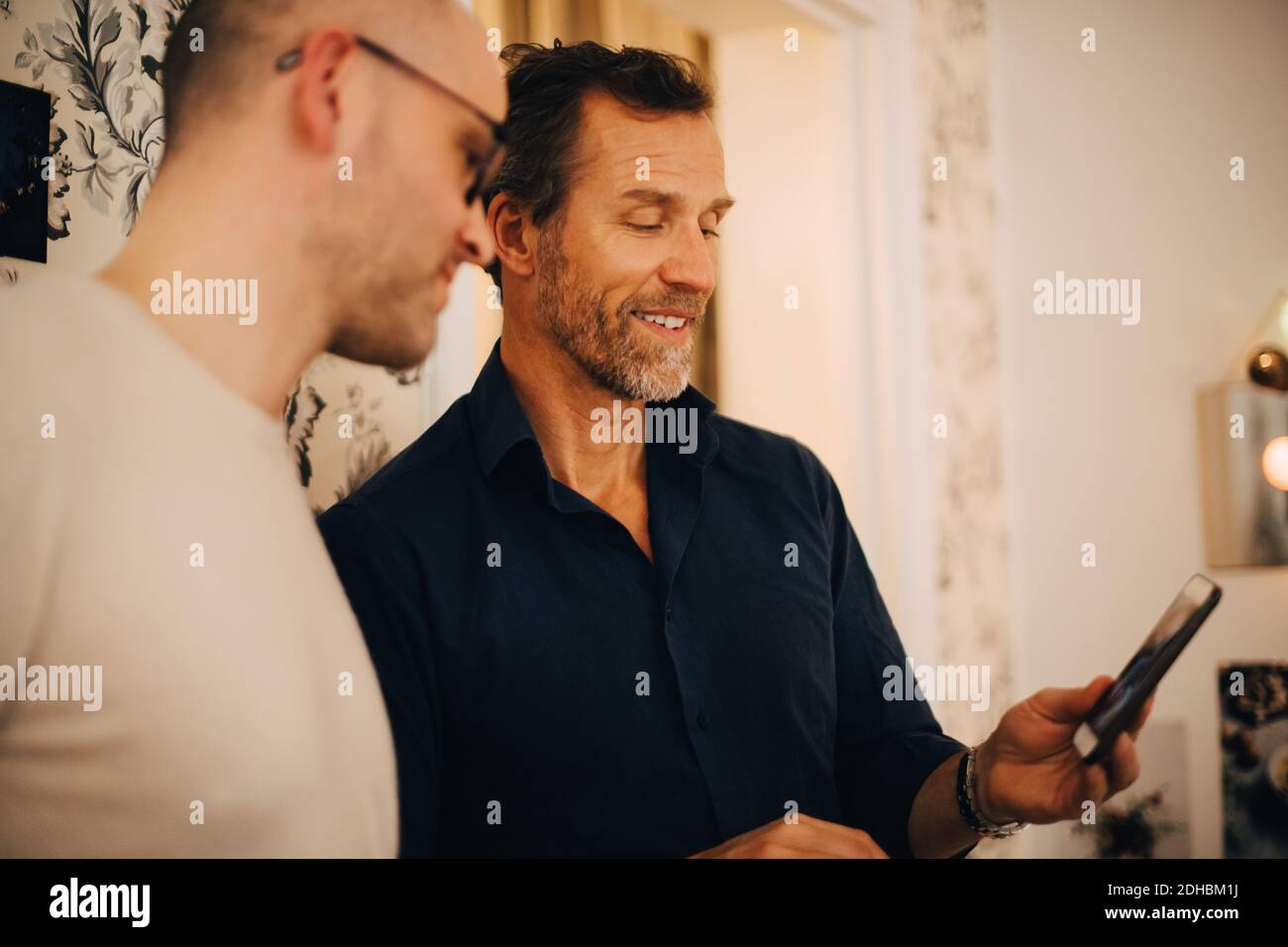 Uomo maturo che mostra il telefono cellulare ad un amico durante la festa a. casa Foto Stock