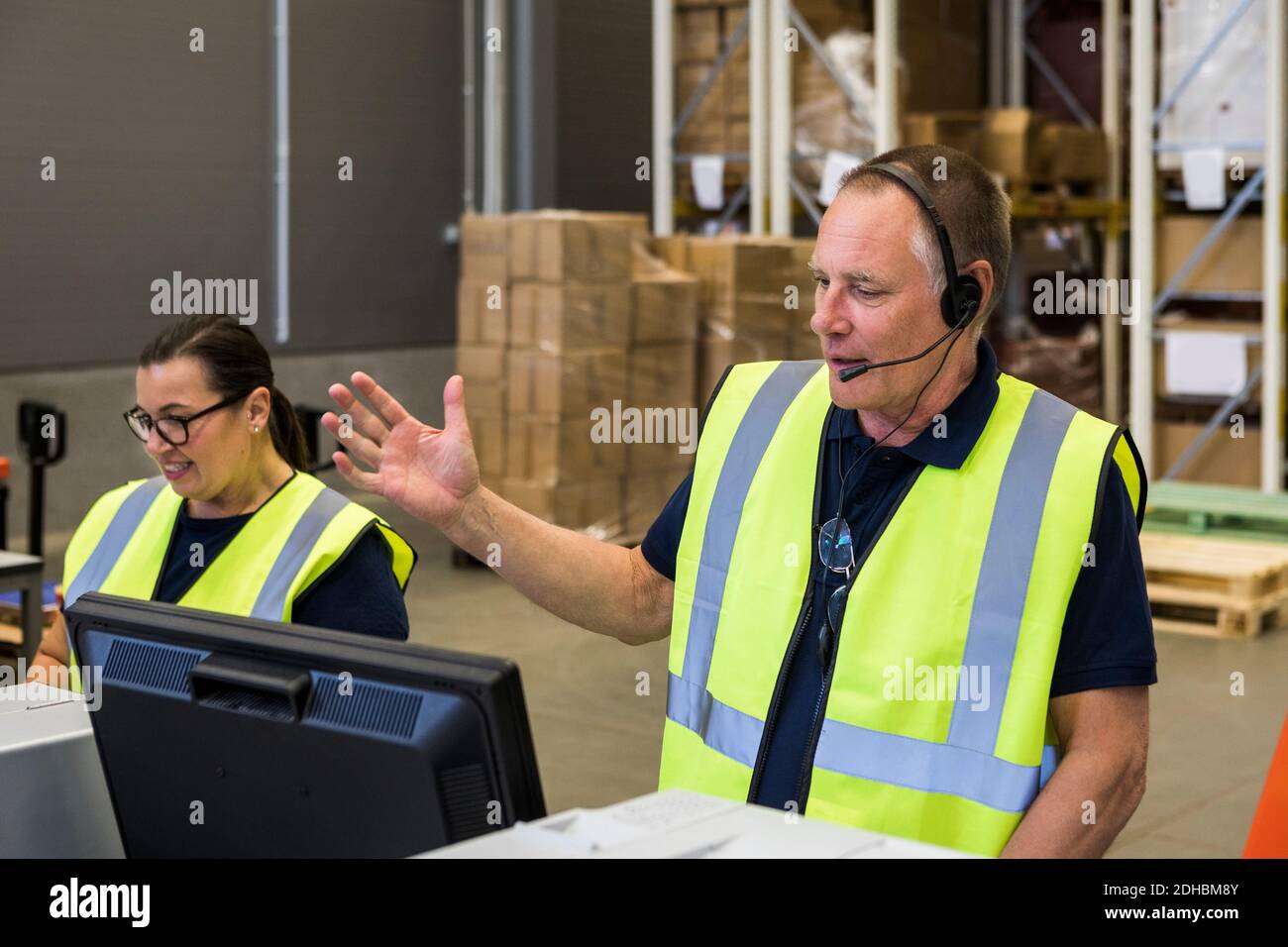 Un esperto dell'assistenza clienti maschile che parla con le cuffie mentre in piedi da una collega femminile in distr Foto Stock