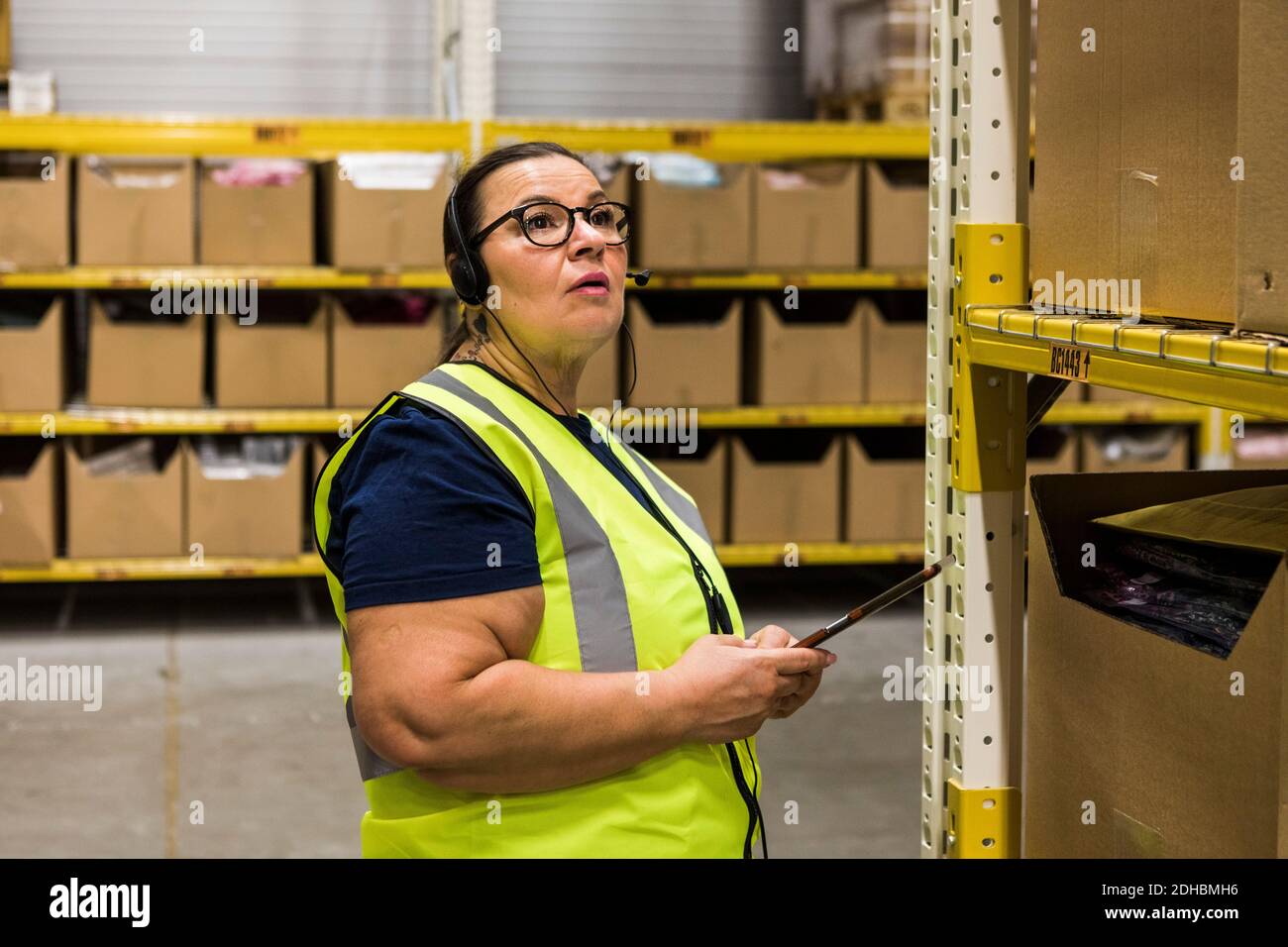 Lavoratrice matura con tablet digitale che guarda lontano mentre parla sulle cuffie presso il magazzino di distribuzione Foto Stock