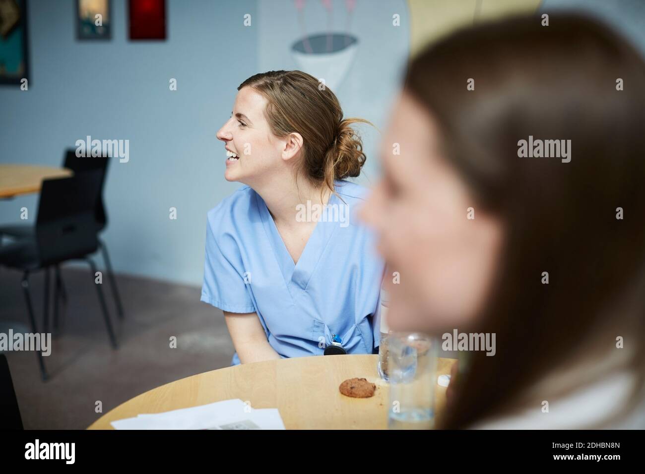 Sorridi le lavoratrici mediche che guardano via mentre si siedono al tavolo in una caffetteria ospedaliera Foto Stock