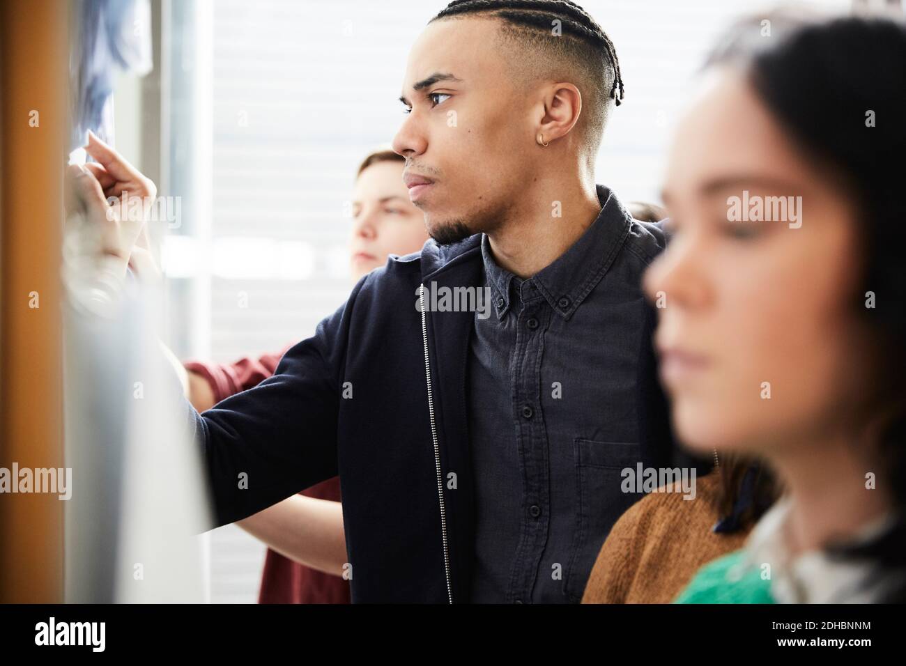 Giovane uomo che controlla i risultati dei test sulla bacheca mentre è in piedi con gli amici all'università Foto Stock