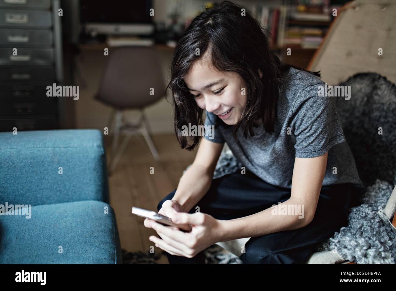 I social media addicted sorridente ragazzo utilizzando il telefono cellulare mentre si è seduti a casa Foto Stock