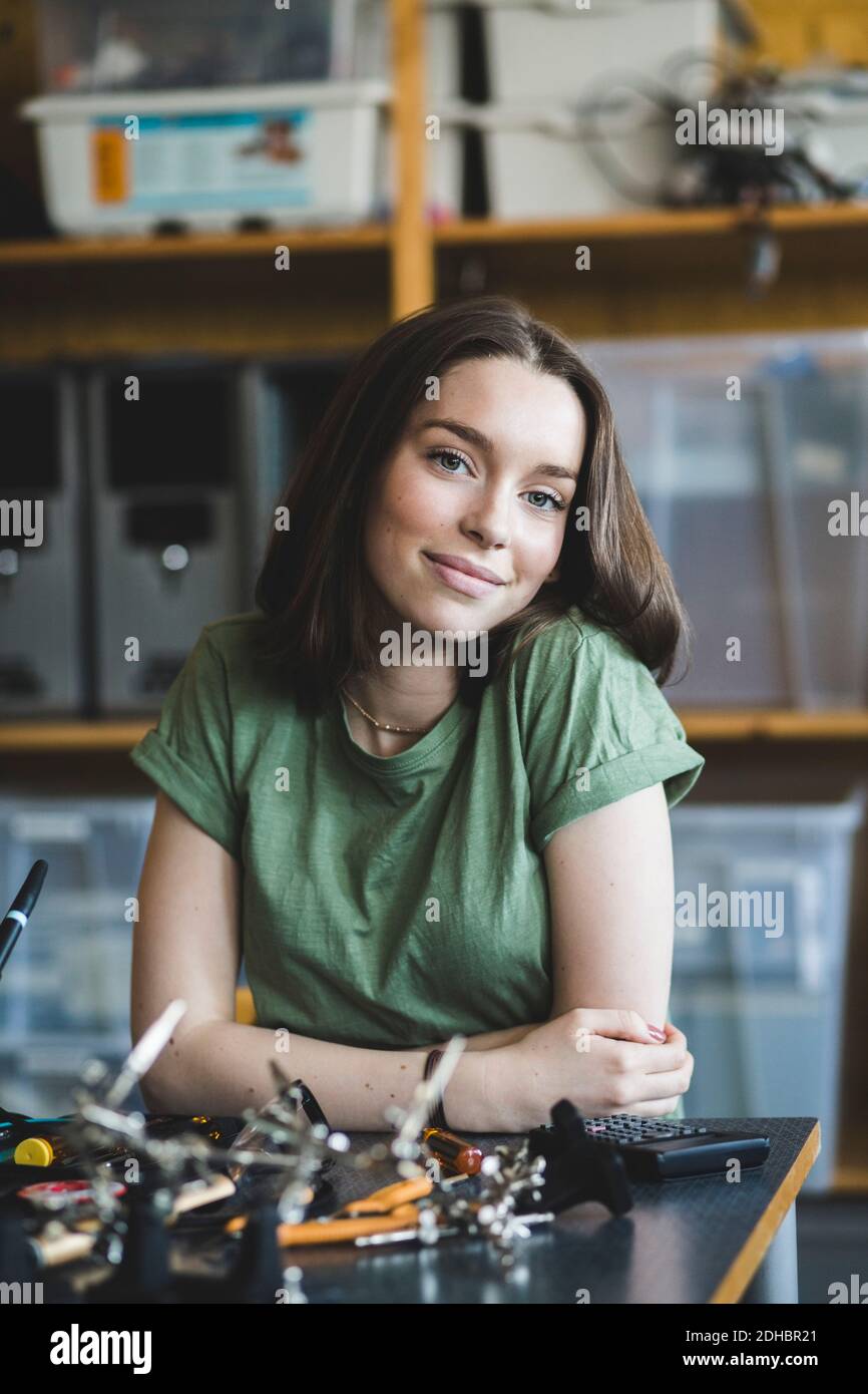 Ritratto di una studentessa sorridente seduta con un progetto scientifico a. scrivania in aula presso la scuola superiore Foto Stock