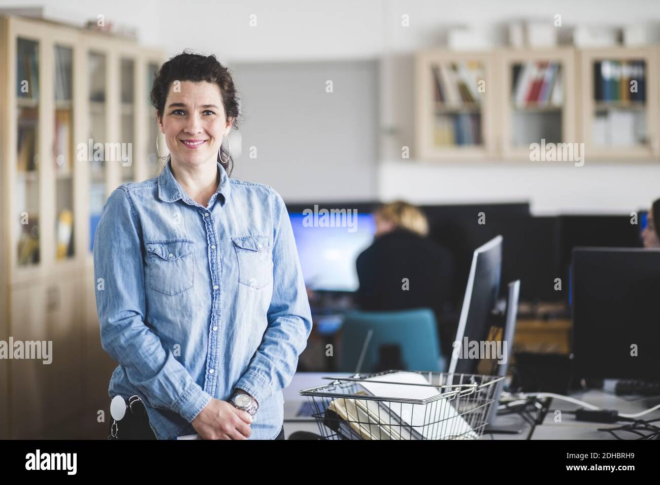 Ritratto di un'insegnante sorridente matura in piedi in laboratorio informatico a scuola superiore Foto Stock