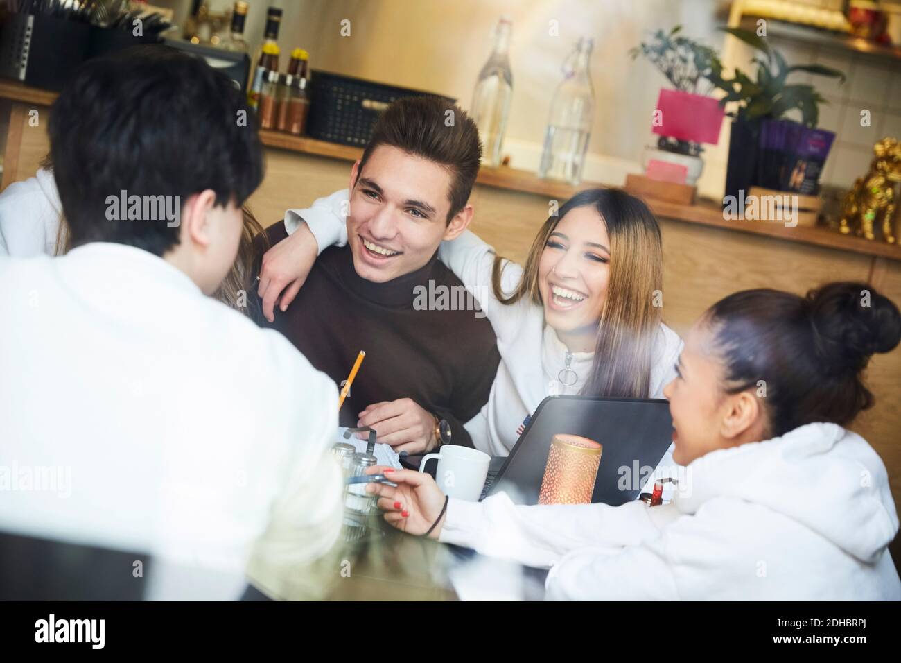 Amici maschi e femmine sorridenti mentre si siedono al tavolo caffè Foto Stock