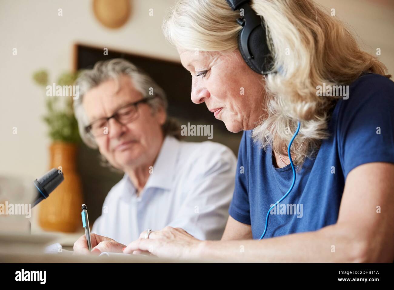 Vlogger senior con cuffie che scrivono mentre si siede con l'uomo a. casa Foto Stock