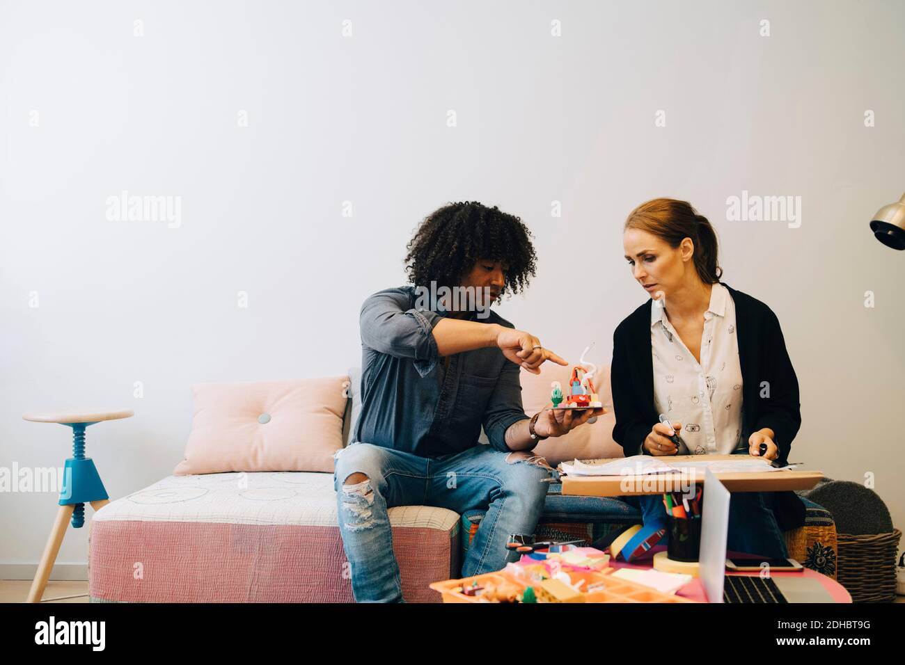 Colleghi aziendali multietnici che discutono del giocattolo mentre si siedono sul divano nella hall dell'ufficio creativo Foto Stock