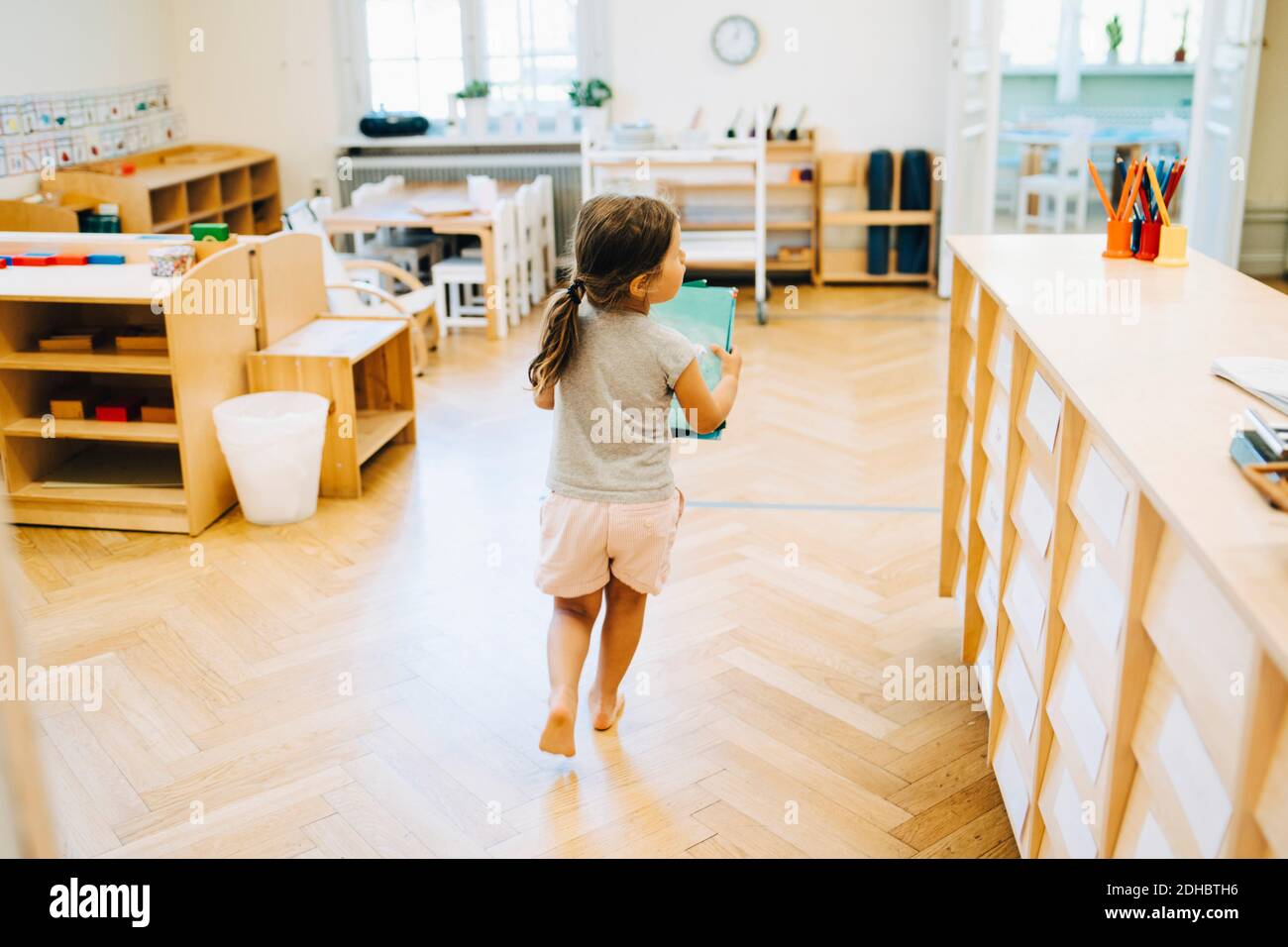 Vista posteriore di lunghezza completa della ragazza che corre con il libro in scuola presso l'asilo Foto Stock