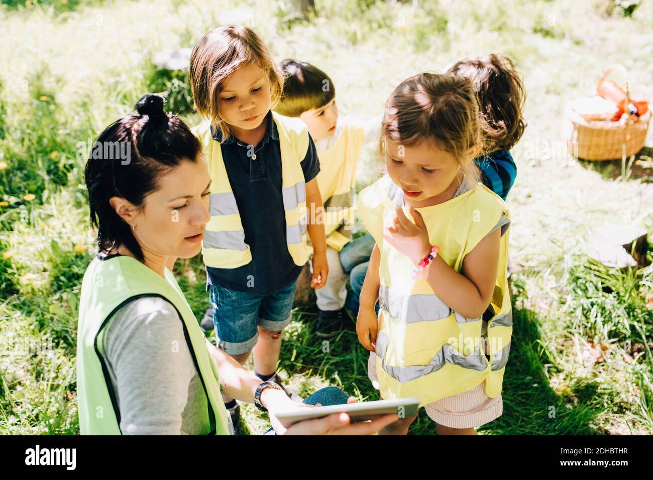 Visualizzazione ad alto angolo di una insegnante di sesso femminile che condivide un tablet digitale con studenti nel parco giochi Foto Stock