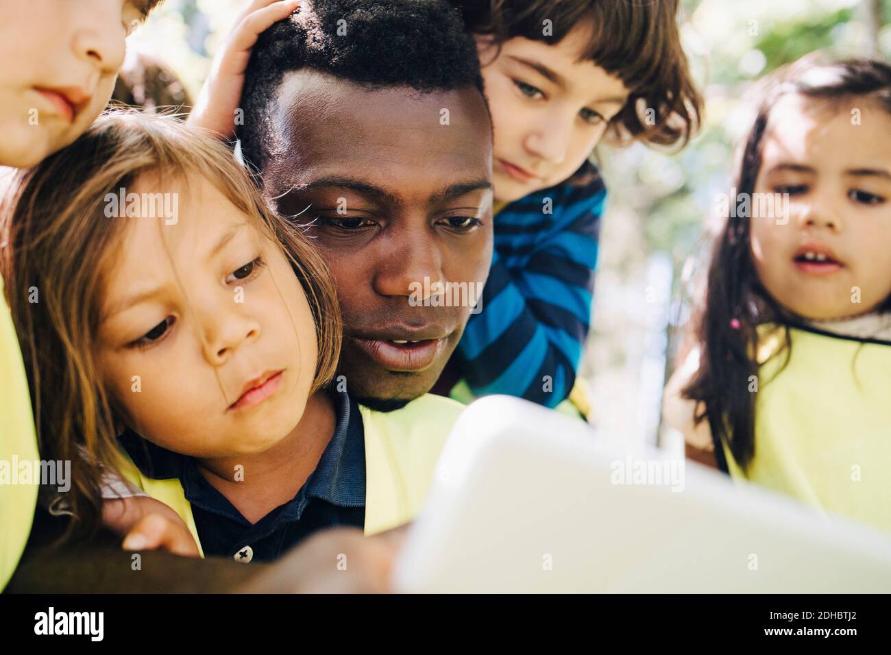 Insegnante di sesso maschile che condivide il tablet digitale con gli studenti nel parco giochi Foto Stock