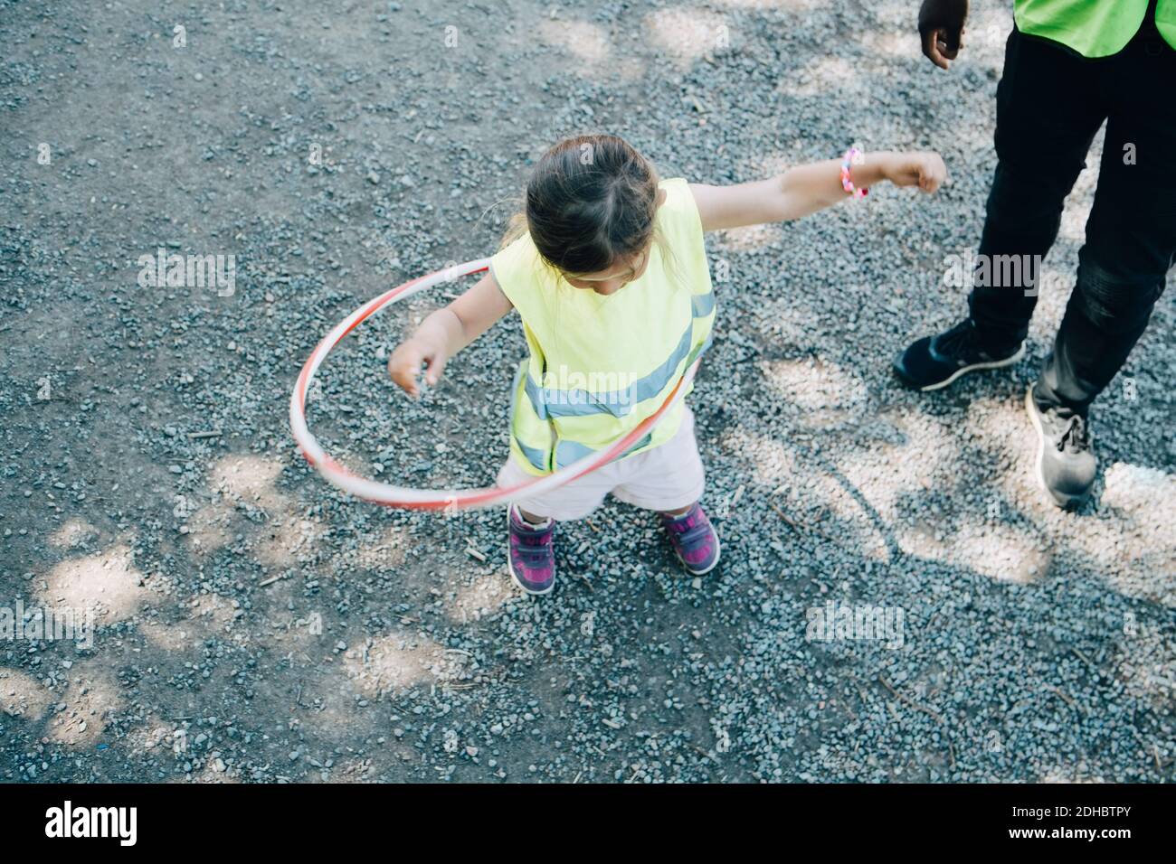 Vista ad alto angolo della ragazza che gioca con cerchio di plastica vicino insegnante di sesso maschile nel parco giochi Foto Stock