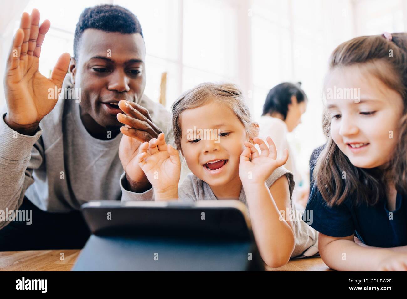 Insegnante giocosa e studentesse che guardano al tablet digitale in aula Foto Stock