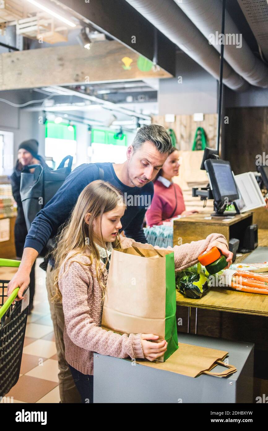 Padre e figlia che imballano i generi alimentari al banco di cassa nel supermercato Foto Stock
