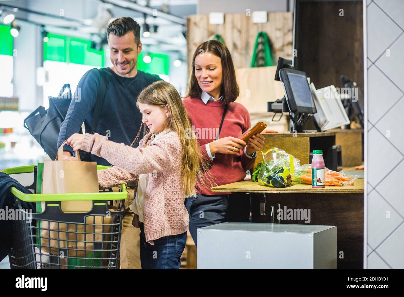 Sorridenti genitori che guardano la figlia che organizza borse di carta nello shopping carrello Foto Stock