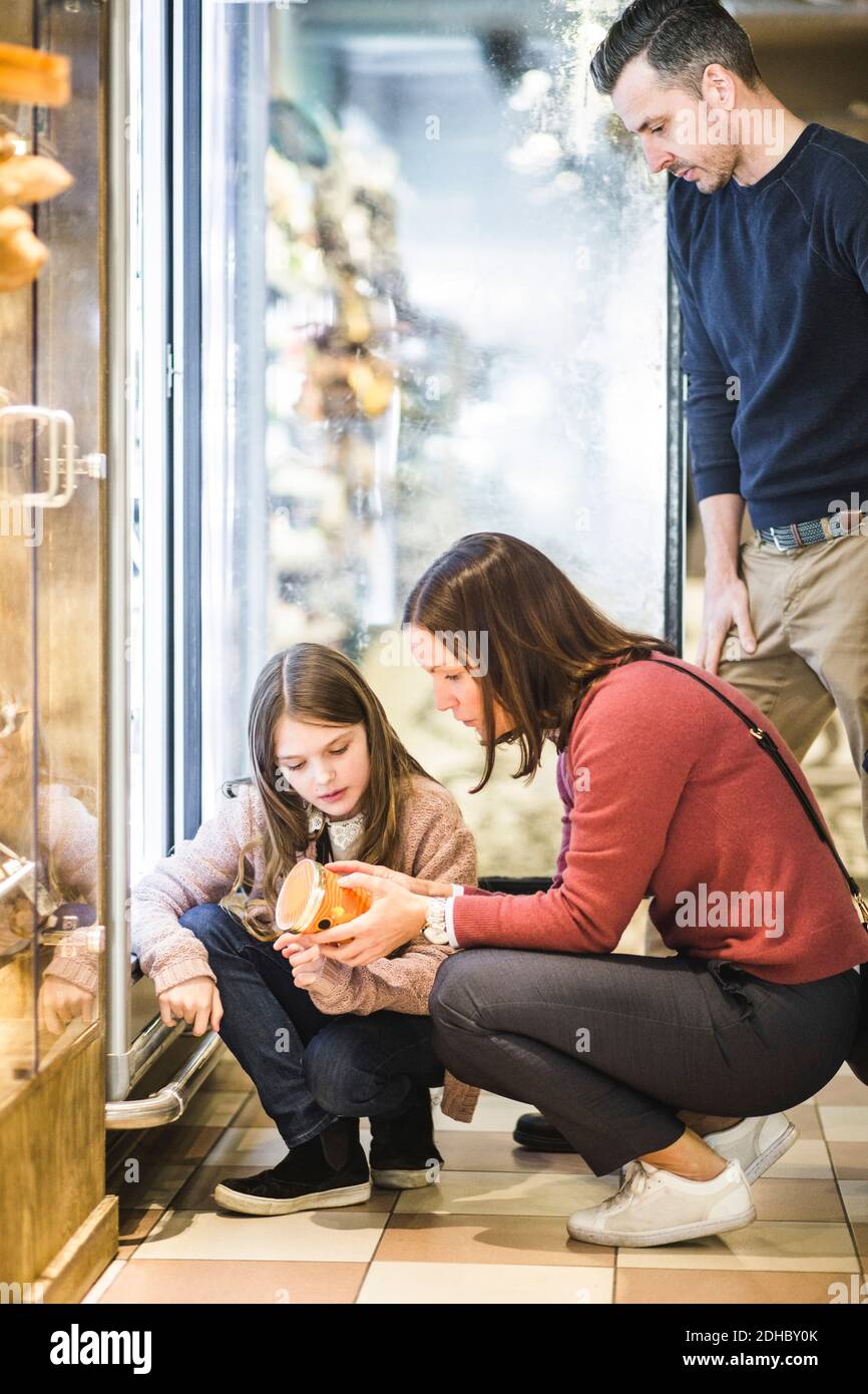 Padre che guarda la figlia e la donna che scelgono il cibo dal frigorifero nel supermercato Foto Stock