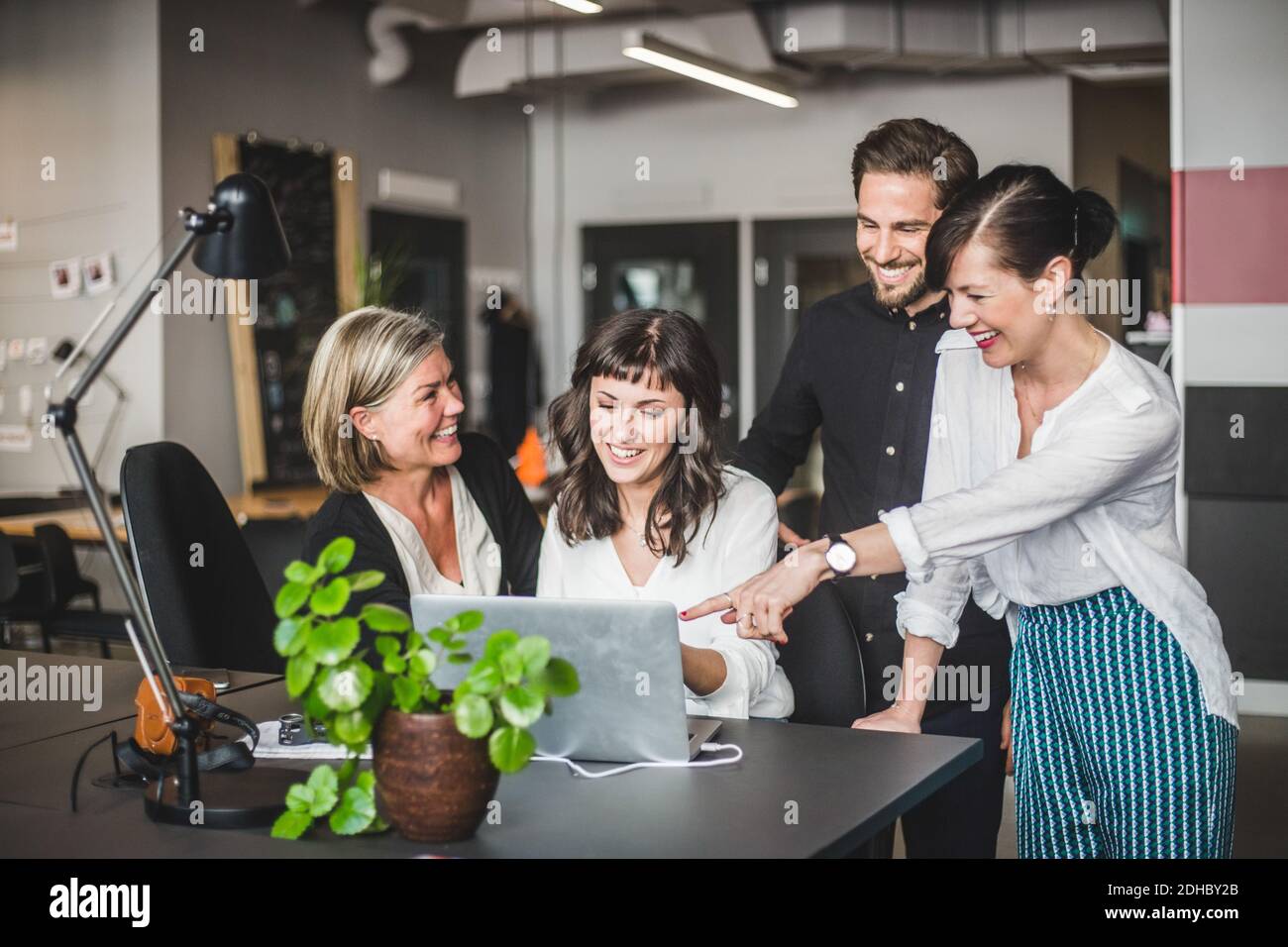Persone creative che sorridono mentre discutono con il computer portatile alla scrivania in ufficio Foto Stock