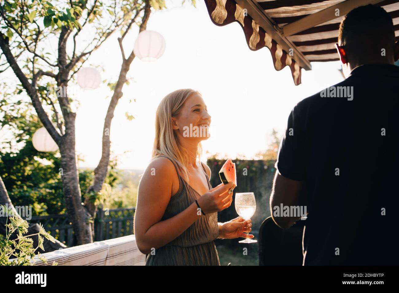Donna che mangia l'anguria e che ha vino mentre parla con un amico in festa Foto Stock