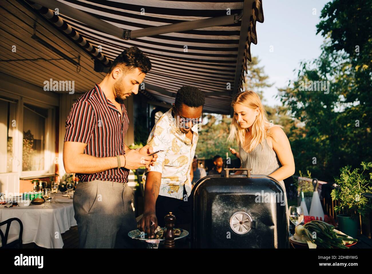 Gli amici parlano mentre gustano il cibo alla griglia durante la festa a cena cortile posteriore Foto Stock