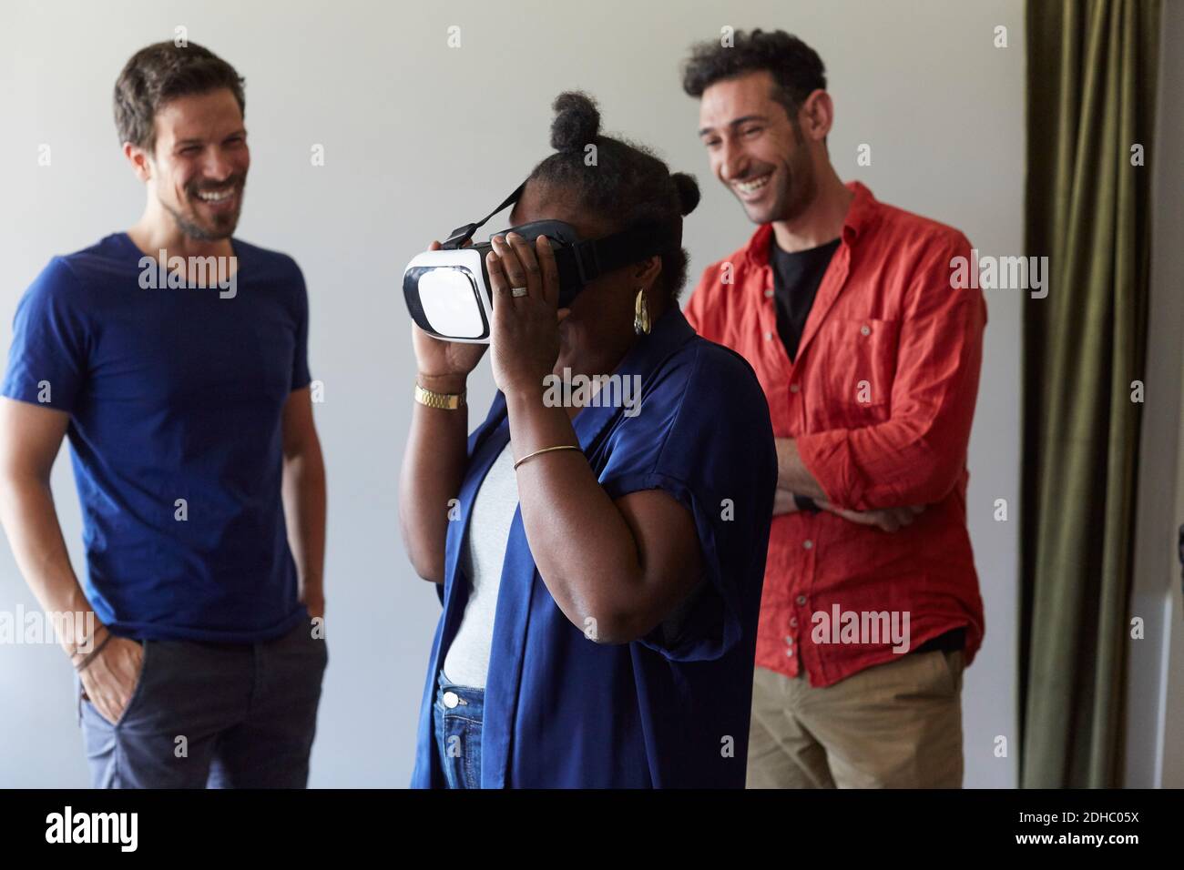 Uomini d'affari sorridono mentre guardano la collega femminile usando la realtà virtuale simulatore in ufficio Foto Stock