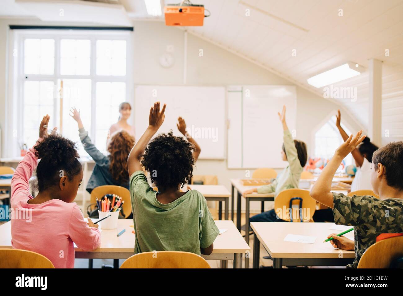 Gli studenti alzano le mani mentre rispondono in classe a scuola Foto Stock